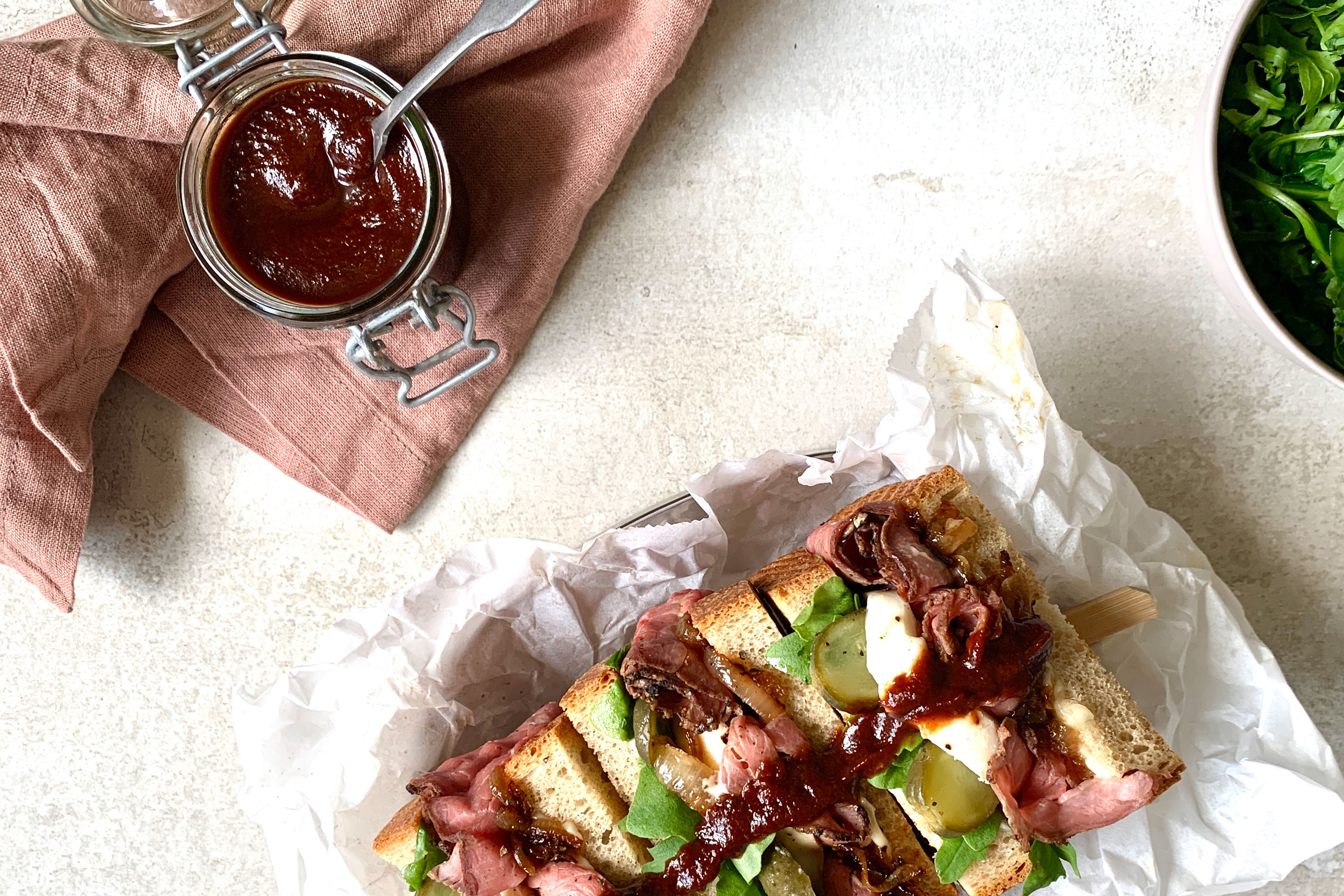 Barbecue-Sauce in einem Einmachglas mit Löffelchen und einem Sandwich